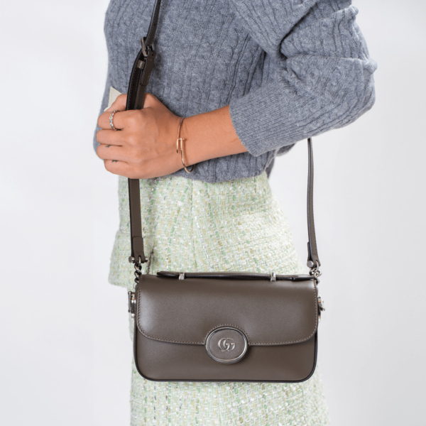 Frau trägt eine kleine braune Ledertasche mit silberner Hardware der Marke Gucci.