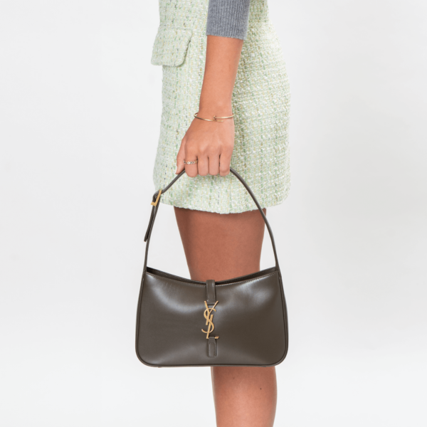 Woman carries a small shoulder bag made of brown leather and golden hardware by Saint Laurent.